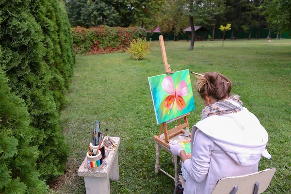 Professional artist woman writes picture sitting at easel with b