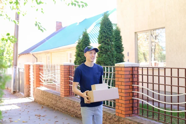 Postman Carring Parcel in Hands Smiling at Camera on Background