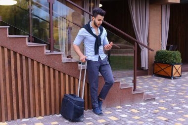 Çekici genç Arap adam elinde bavulla ayakta ve p