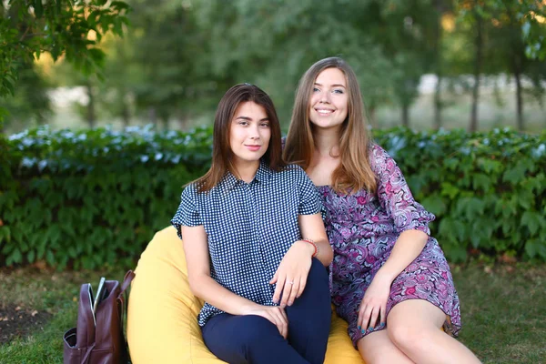 Duas meninas atraentes sentadas ao lado umas das outras na cadeira, sorrir — Fotografia de Stock