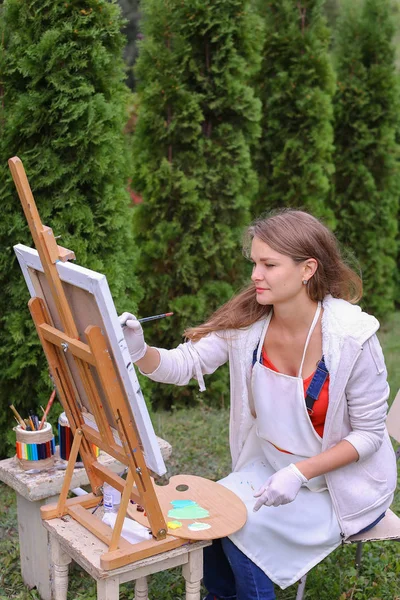 Girl artist paints picture and sits on chair at easel sides of t — Stock Photo, Image