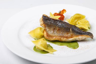 Beyaz ve sarı balık mantı yeşil soslu beyaz b plaka üzerinde