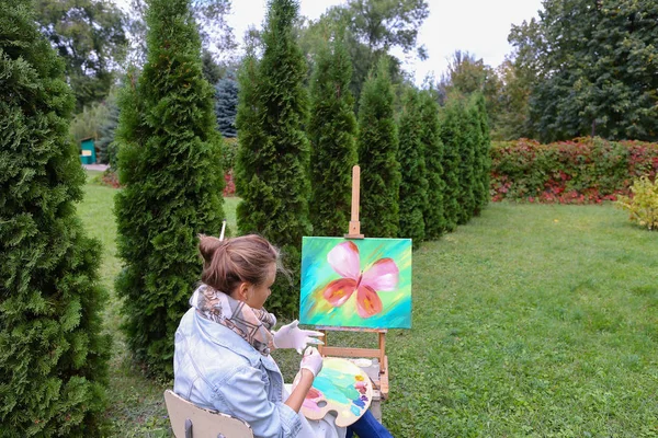 Professional artist woman writes picture sitting at easel with b