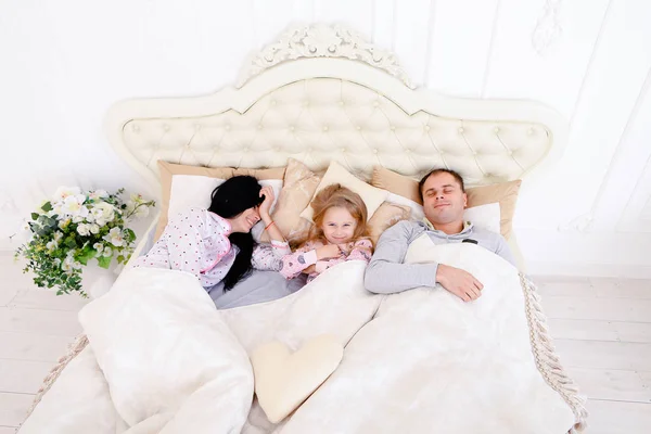 Família feliz deitada em uma cama branca e dormir. Mãe, pai e — Fotografia de Stock