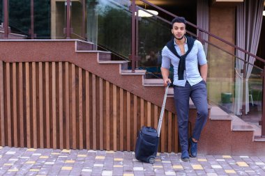 Çekici genç Arap adam elinde bavulla ayakta ve p