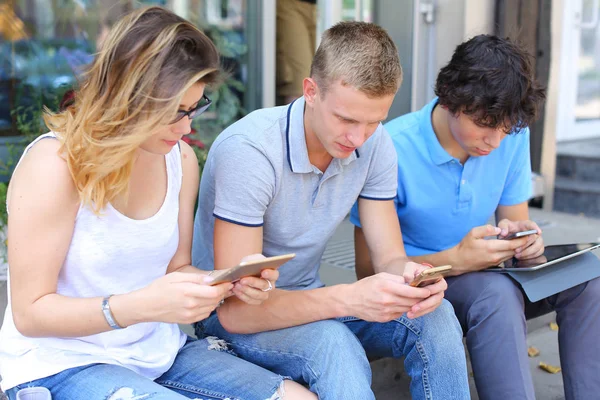Молодые трое друзей сидят на улице, разговаривают, используют — стоковое фото