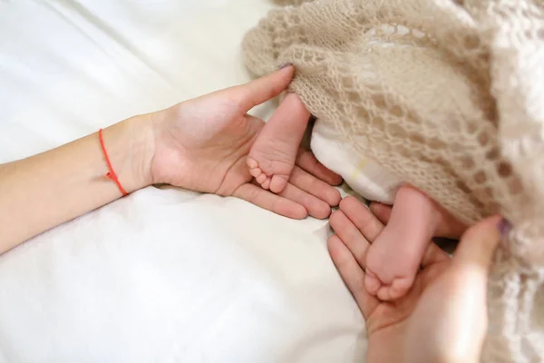 Mamusie, trzymając w rękach małe stopy noworodka, pokryte knitte — Zdjęcie stockowe