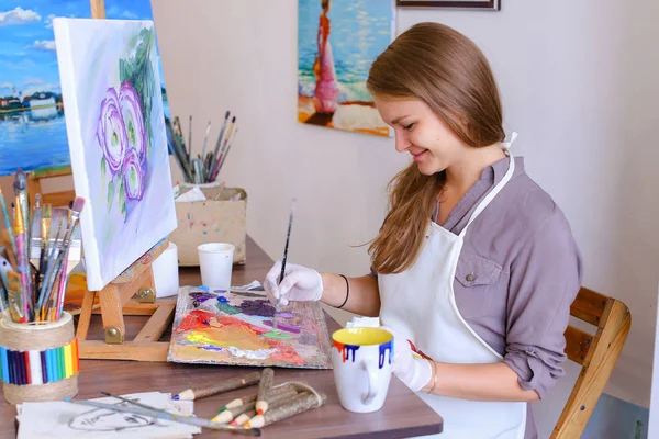 Chica se sienta en el taburete en el caballete y escribir pintura, utiliza el pincel para —  Fotos de Stock