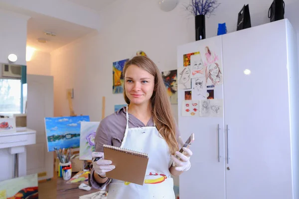 Chica artista sosteniendo el teléfono móvil y el uso, hablar, escribir pluma o —  Fotos de Stock