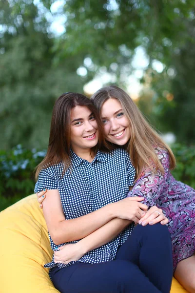 Dos chicas atractivas sentadas una al lado de la otra en silla, smilin —  Fotos de Stock