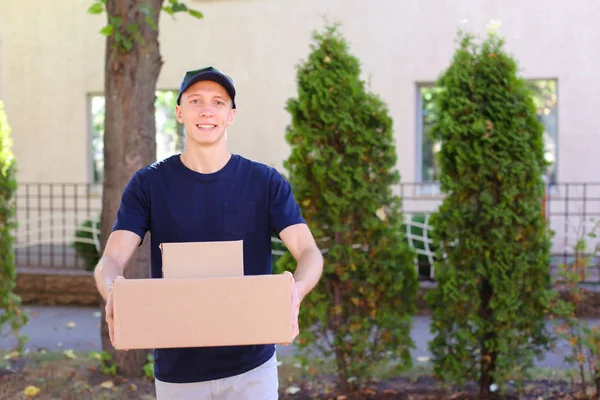 Joven mensajero llevando la orden en las manos, sonriendo a la cámara y — Foto de Stock