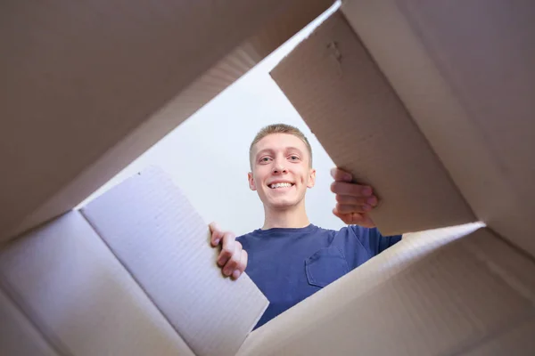 Joven abre caja de cartón marrón, mirando en la cámara sonriendo una — Foto de Stock