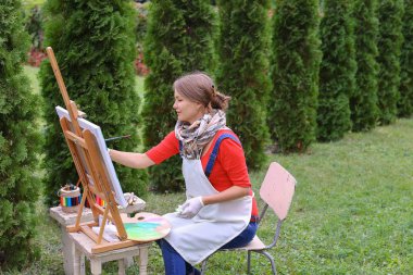 Kız sanatçı boya resim ve t kenarlarında şövale sandalyeye oturur