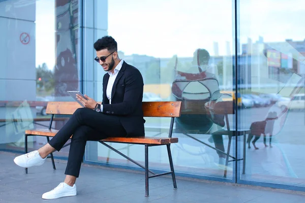 Hombre de traje árabe se pone gafas de sol con tableta cerca de negocios — Foto de Stock