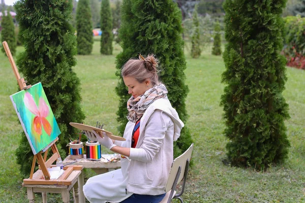 Kız sanatçı boya resim ve t kenarlarında şövale sandalyeye oturur — Stok fotoğraf