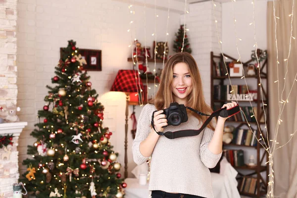 Menina atraente jovem sorrindo com covinhas e segurando cameraphotographer em uma árvore de Natal fundo — Fotografia de Stock