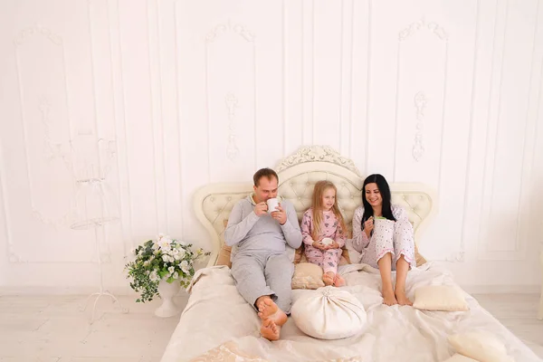 Gelukkige familie thee of koffie drinkt in pyjama glimlachen en op zoek — Stockfoto