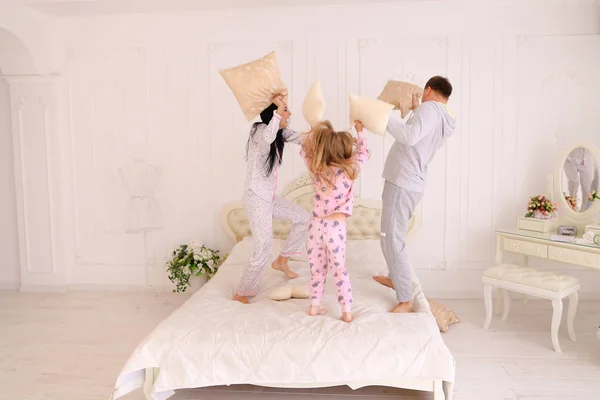 Retrato de família lutando travesseiros, pulando na cama juntos em — Fotografia de Stock