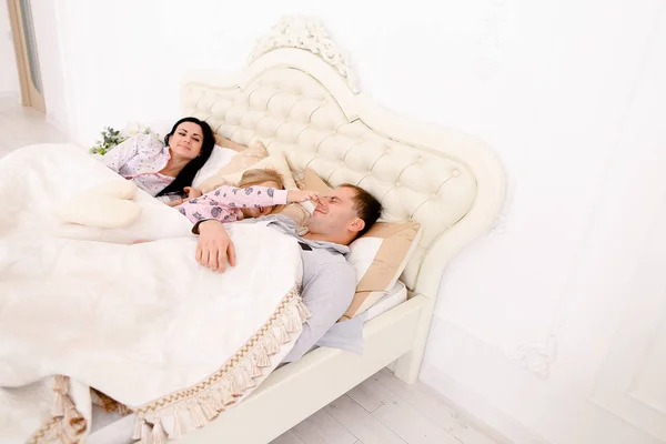 Mamma, papa 'si e' svegliato. Famiglia felice sdraiata in un letto bianco — Foto Stock