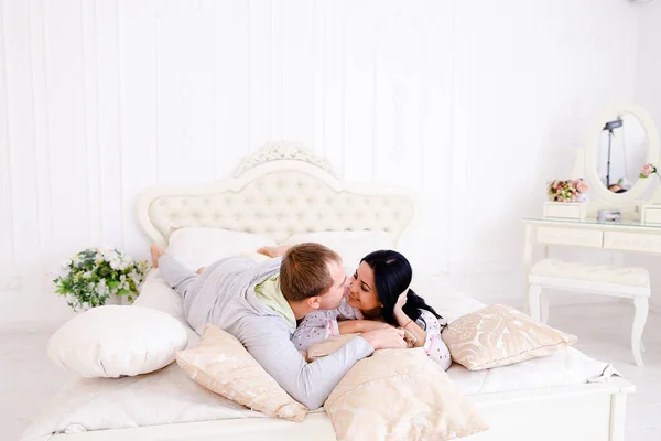 Mąż tulenie żonę w łóżku z samego rana w białym pokoju — Zdjęcie stockowe