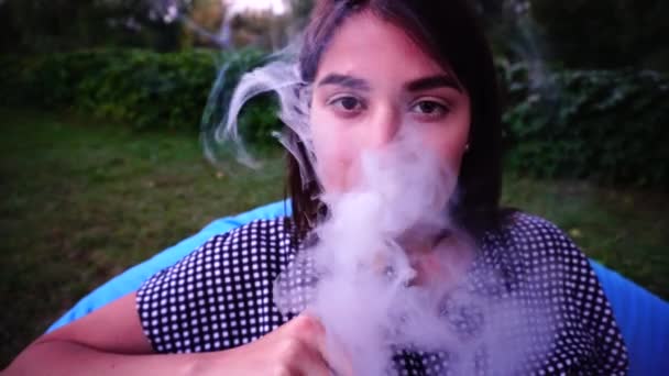 Meisje op mysterieuze wijze op zoek naar Camera zonder gezicht en rook Hookah, zittend in de stoel in Park in openlucht. — Stockvideo