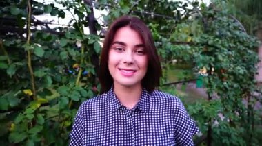 Güzel kız öğrenci görünüyor ve kamera gülümsüyor duruyor Park'ta açık havada öğleden sonra.