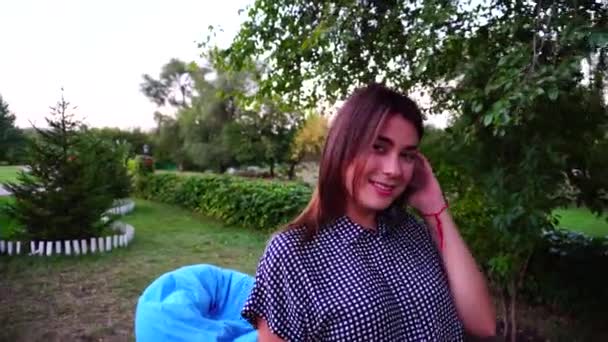 Elegante chica mira a la cámara con sonrisa y paseos en el parque al aire libre en el día . — Vídeos de Stock