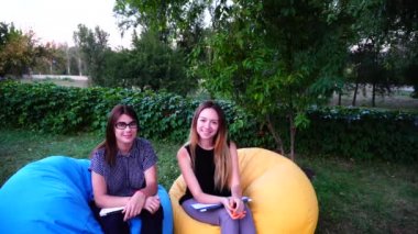 Güzel kadın kadın çalışanların gülümseme kamera ve hareket göstermek, oturup birlikte koltuklar Park'ta açık hava sırasında gün içinde.