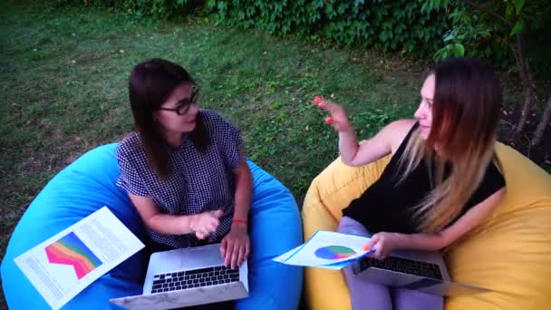 Két női webes tervezők, akik Design webes felületek helyek ül a parkban szabadtéri Park nap folyamán portréja. — Stock videók