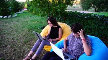 Zeki kızları hizmet mühendisleri yazılım hizmetleri ve destek programları, koltuklar içinde gündüz parkta otururken dizüstü bilgisayarlar ile çalışma yapan.