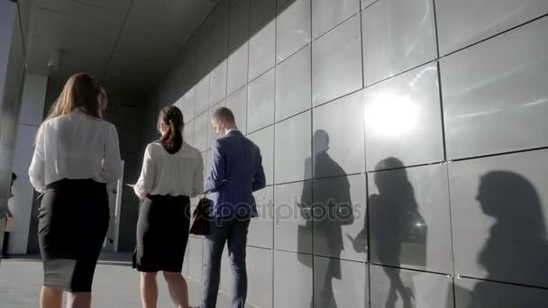 Weibliche und männliche Büroangestellte gehen zurück zur Kamera und sprechen über Arbeitspapier auf dem Hintergrund der Wand des Business Centers im Freien in neutralen Farben. — Stockvideo