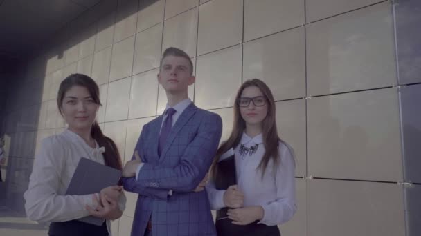 Tres jóvenes empresarios educados posando en la cámara con la carpeta en las manos en el fondo de la pared cerca del centro de negocios al aire libre en colores neutros . — Vídeos de Stock