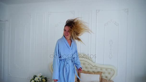 Retrato de la mujer saltando en la cama, levanta los brazos disfruta bailando y sonriendo gran sonrisa en el dormitorio brillante . — Vídeo de stock