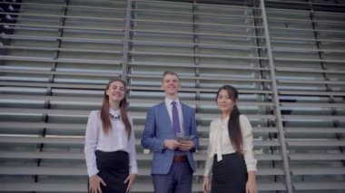 Üç kendine güvenen genç insanlar öğrenciler kağıt dağılım ve gülümseyen ve gülüyor, başarı, iş merkezinin nötr renklerde açık havada duran sevinirler.