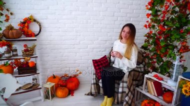 Güzellik rahatla ve beyaz duvar odadaki sonbahar dekorasyonları ile dekore edilmiş karşı sandalyede oturup çay içecek.