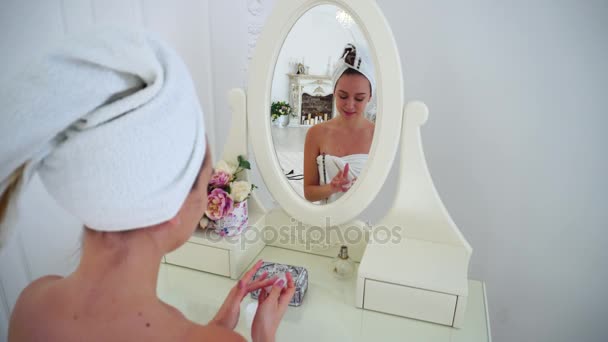 Dona de casa bonita do chuveiro, hidrata a pele com creme para rosto e sorri na reflexão no espelho no quarto brilhante . — Vídeo de Stock