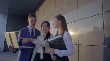 Üç güzel gençler, öğrenciler ellerinde tutmak Laptop ve klasörleri arka plan açık havada nötr renklerde iş merkezinin konuşurken,.