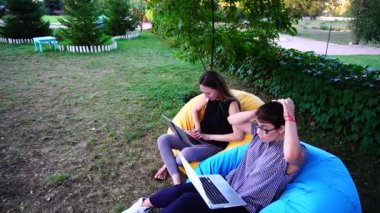 Kadın satış yöneticileri değil var tüm iş ve hızlı bir şekilde türü bilgisayar klavye oturan yumuşak sandalyeler havada Park içinde gündüz vakti yapmak.
