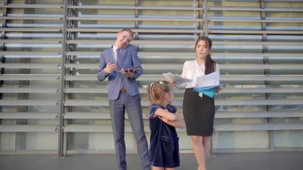 Di Foreground Stands Little Girl and Angry, di Background Young Women and Man Talking on Phone and Stand Near Business Center in Neutral Colors . — Stok Video