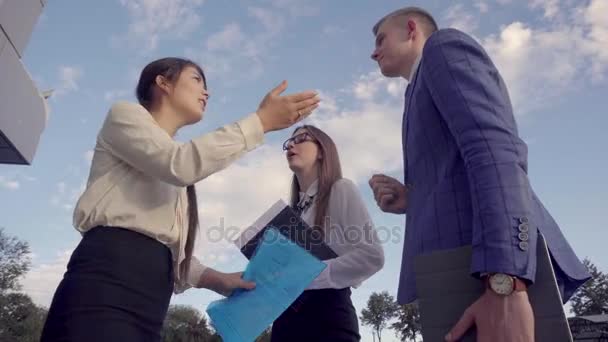 Jóvenes empresarios comparten ideas y estrechan las manos, se paran cerca del centro de negocios contra el trasfondo del cielo al aire libre en colores neutros . — Vídeo de stock