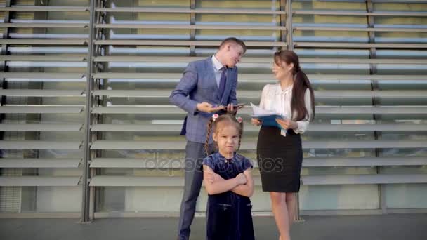 Im Vordergrund steht ein kleines Mädchen auf dem Hintergrund Frauen und ein schöner Mann auf dem Hintergrund eines Business Centers im Freien in neutralen Farben. — Stockvideo
