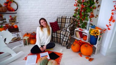 Kız serbest meslek belgeleri ve gülümseyen ve beyaz duvar odadaki sonbahar dekorasyonları ile dekore edilmiş karşı katta oturan grafiklerinde, çalışma.