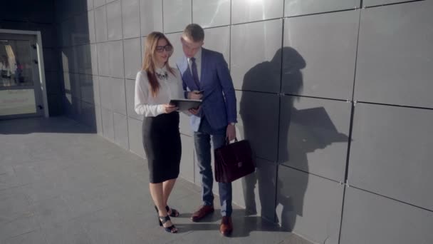 Hombre de negocios guapo hablando con la dama de negocios y sosteniendo documentos en las manos en el fondo del centro de negocios en colores neutros . — Vídeos de Stock