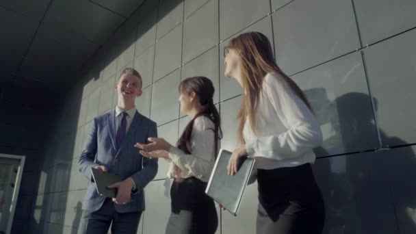 Aantrekkelijke opgeleide jonge studenten praten en glimlachen, lachen en staan op de achtergrond van de muur in de omgeving van Business Center buiten in neutrale kleuren. — Stockvideo