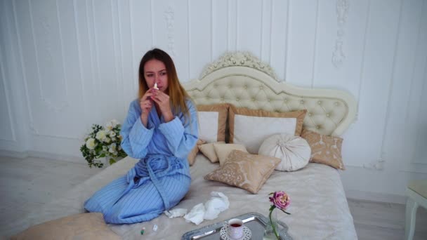 Mujer joven en condición poco saludable tratada con medicamentos farmacéuticos, sentada en una cama grande en el dormitorio . — Vídeos de Stock