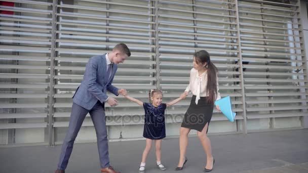 Mladá moderní rodina směje, drželi se za ruce a stojící na pozadí obchodní centrum venku v neutrálních barvách. — Stock video