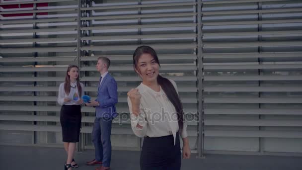 Bella studentessa sorridente e in posa davanti alla macchina fotografica, mostra gesti e bancarelle sullo sfondo dei colleghi vicino al centro commerciale in colori neutri . — Video Stock