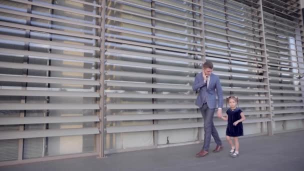 Zakenman, jonge vader praten op telefoon en Leads meisje met de Hand, wandelen samen langs ramen van Business Center buiten in neutrale kleuren. — Stockvideo