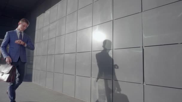 Jovem Gerente Masculino Caminha Junto e Olha para Relógio à Mão no Fundo do Centro de Negócios Ao Ar Livre em Cores Neutrais . — Vídeo de Stock