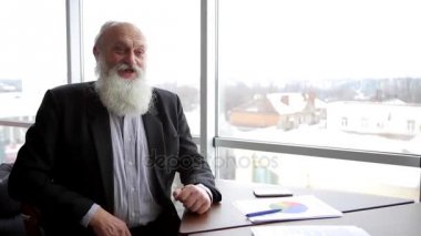 Yaşlı adam yönetmen adam kamera ve öğleden sonra Office büyük pencereler yakınındaki masada oturan gülümsüyor, arkasındaki adam ile iletişim kurar